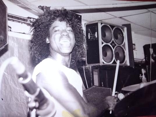 Young Robert with sticks in front of speaker stacks